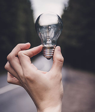 an image of a human hand holding a lightbulb between forefinger and thumb